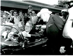 Dave Garroway driving the car. Shaking hands with unknown man.