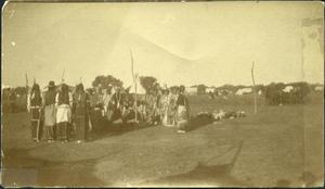 group of Indians in a circle with white tents in the background