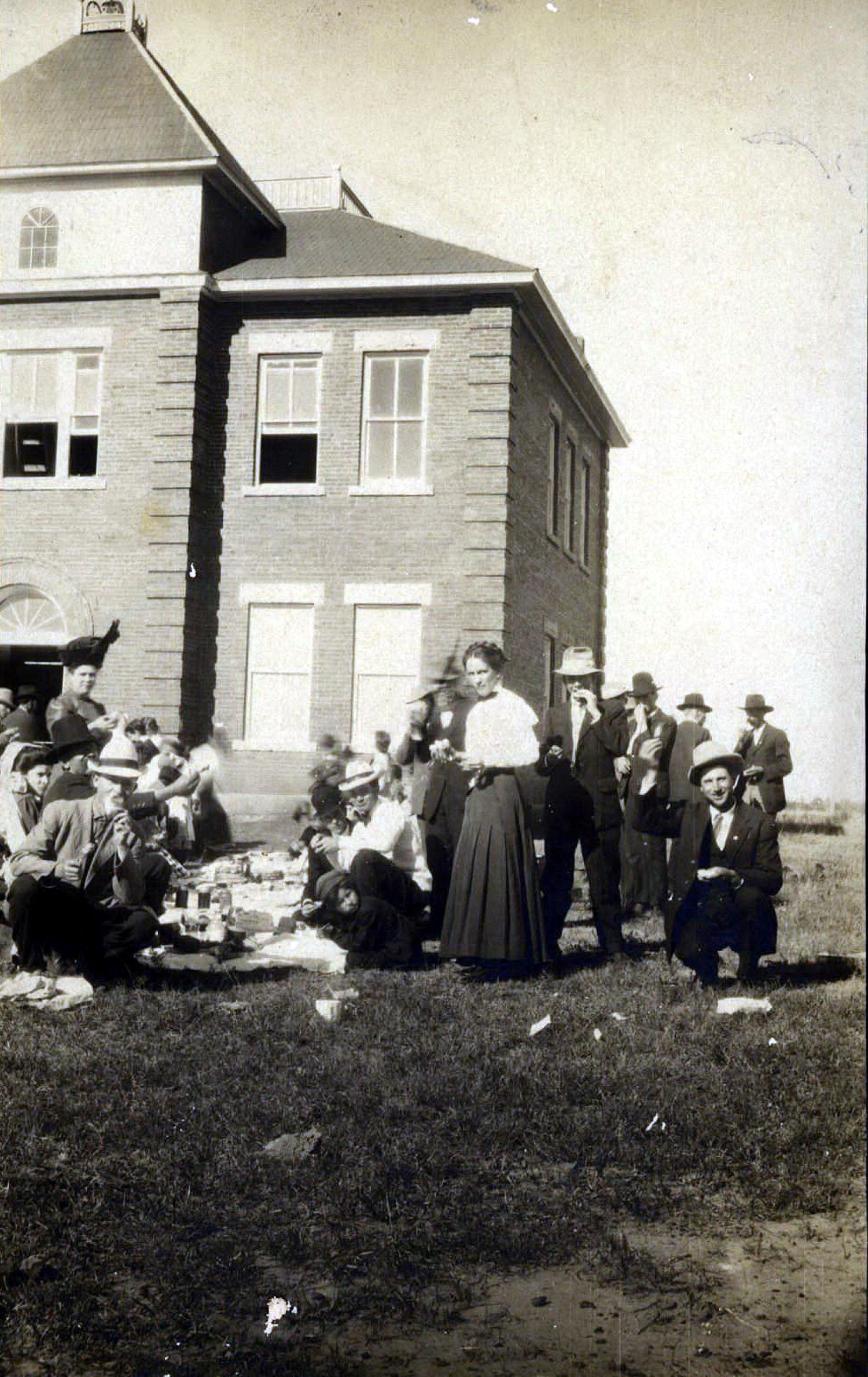 Group of students and teachers outside a school seen having a picnic.
                                                
                                                    [Sequence #]: 1 of 1
                                                